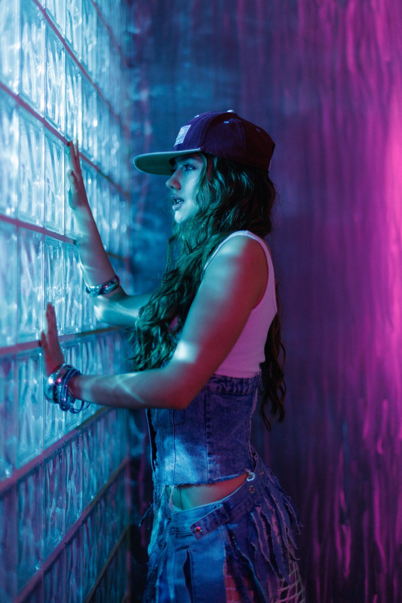 Jelexy reaching toward a glass-block wall, lit in pink and blue